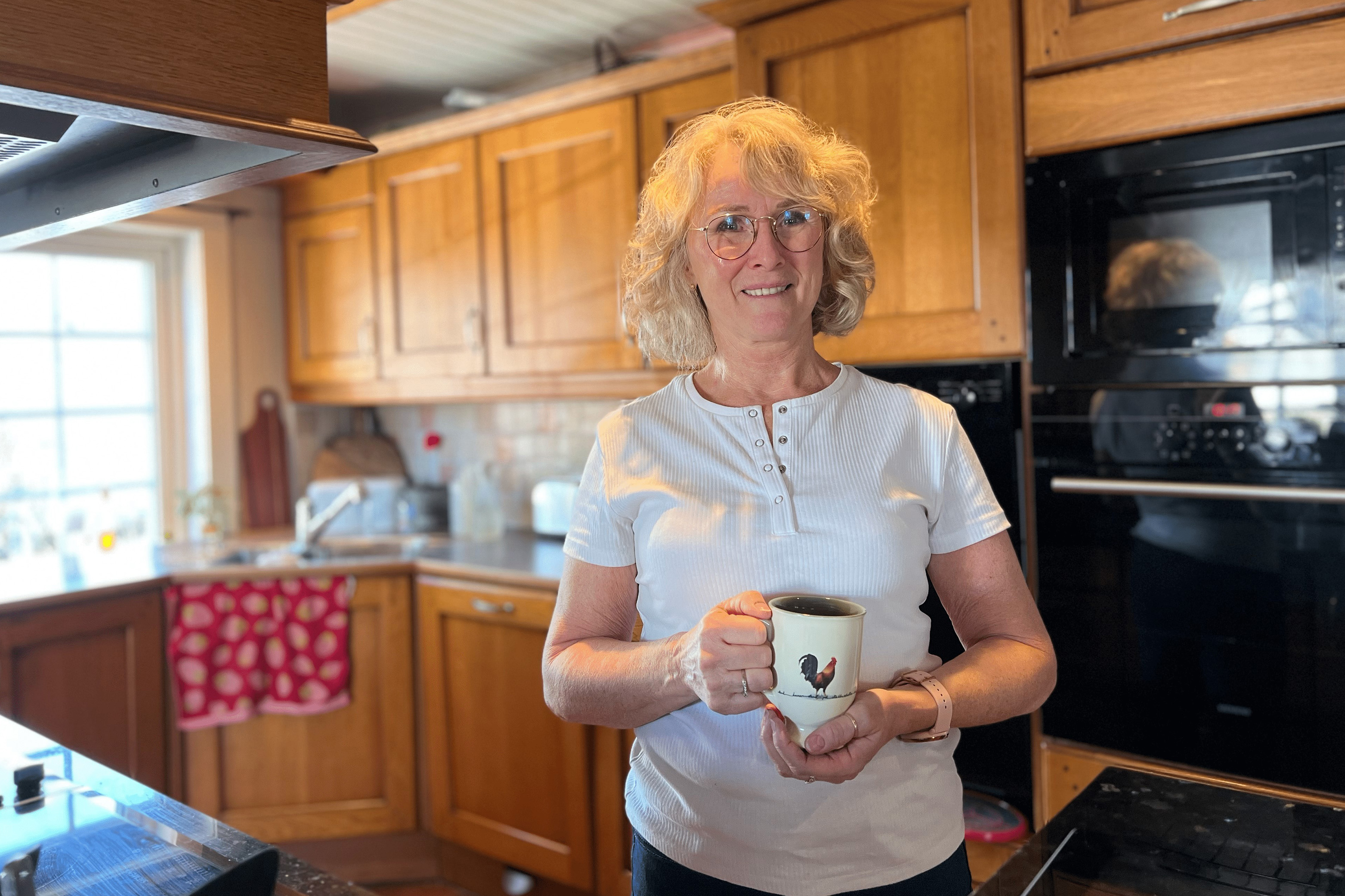Anne står på kjøkkenet med en kaffekopp i hånda