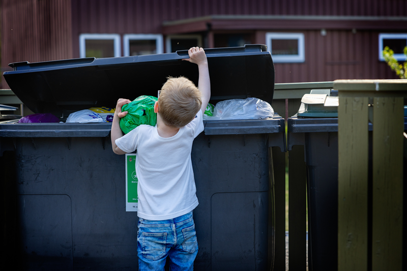 Gutt kaster søppelpose i søppelkasse.