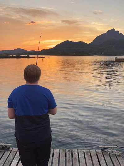 En ung gutt står med ryggen til og fisker med solnedgangen i bakgrunnen